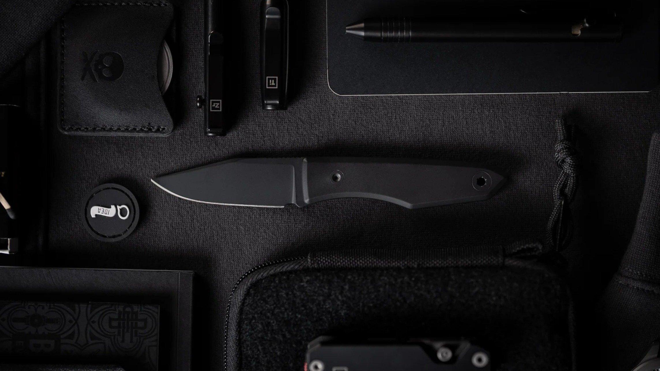 Big Idea Design Lookout EDC knife with black Cerakote coating on a black background, surrounded by black EDC tools