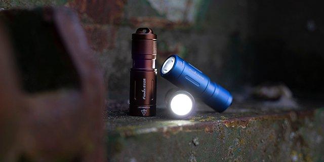 Tres linternas llavero de diferentes colores encendidas sobre una roca