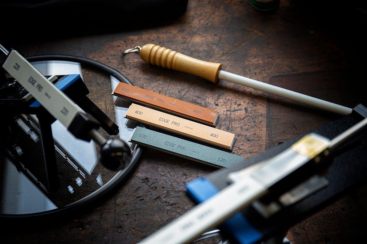 Trois pierres d'aiguisage Edge Pro de différentes granulométries. De haut en bas : grain 600, grain 400 et grain 120. On voit à côté un système d'aiguisage ainsi qu'un fusil d'aiguisage.