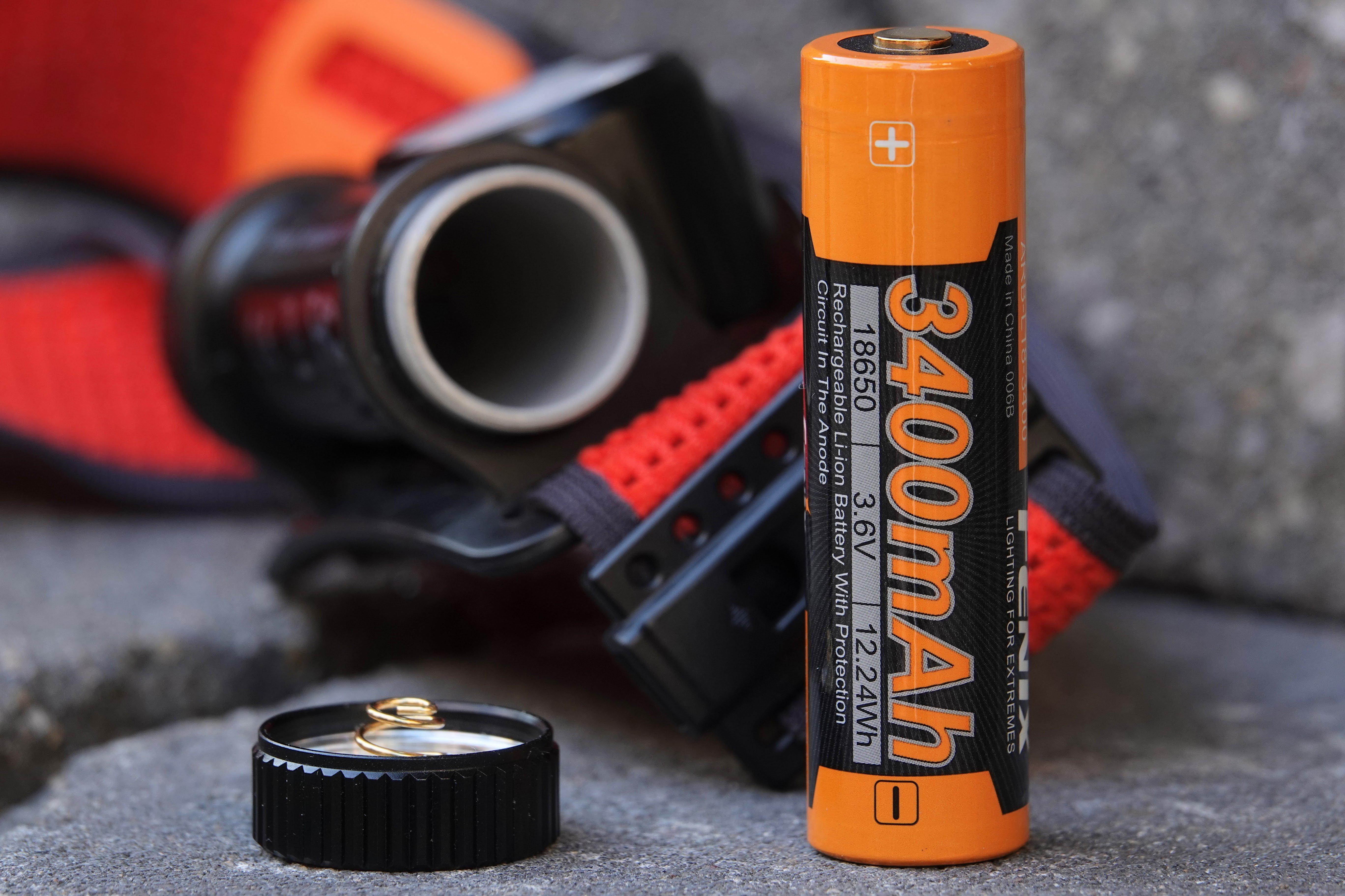 Fenix HM65R-T V2.0 zaklamp op de achtergrond met de batterijopening open. 3400 mAh batterij op de voorgrond.