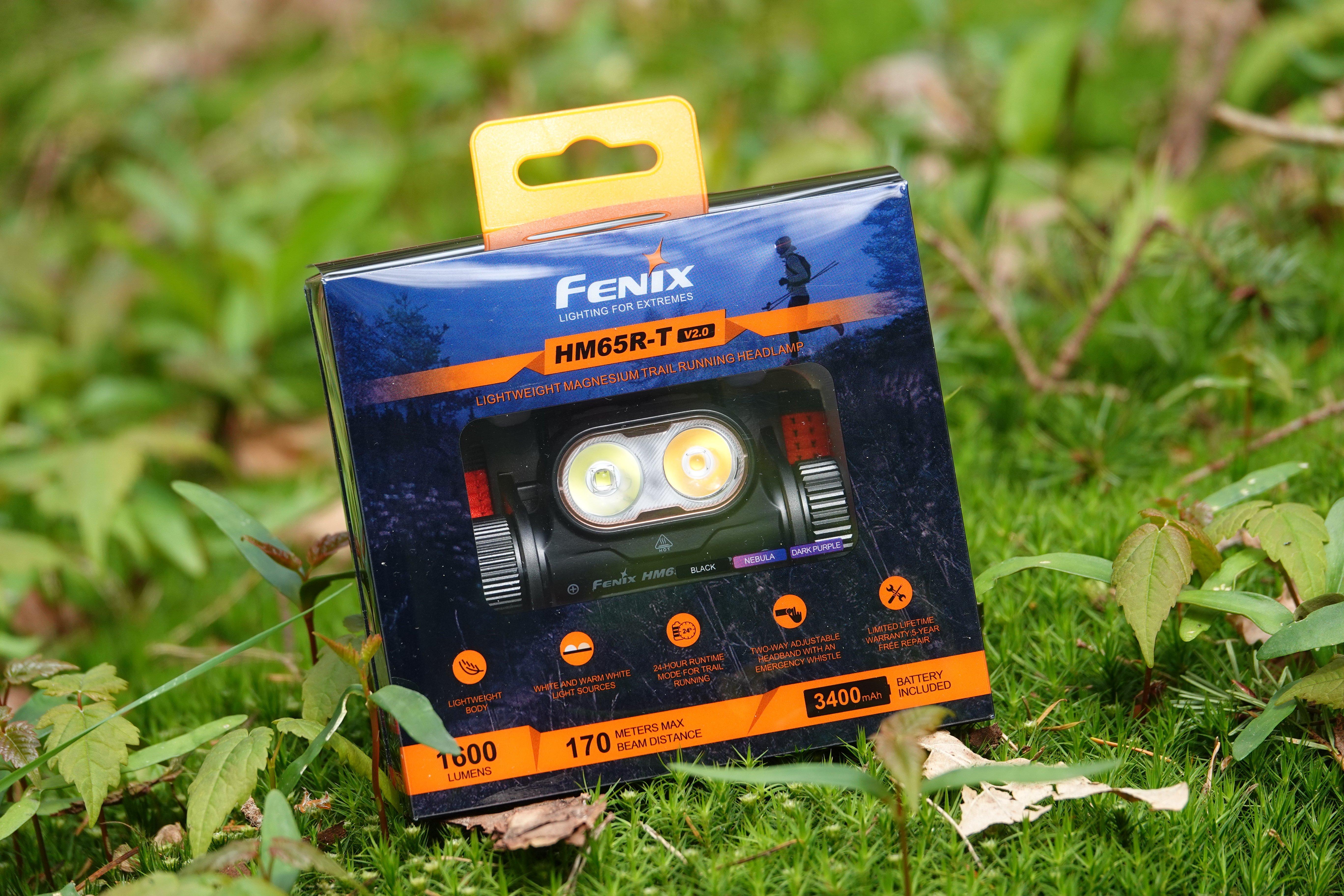 De Fenix HM65R-T V2.0-hoofdlamp in zijn plastic verpakking, op een groene weide