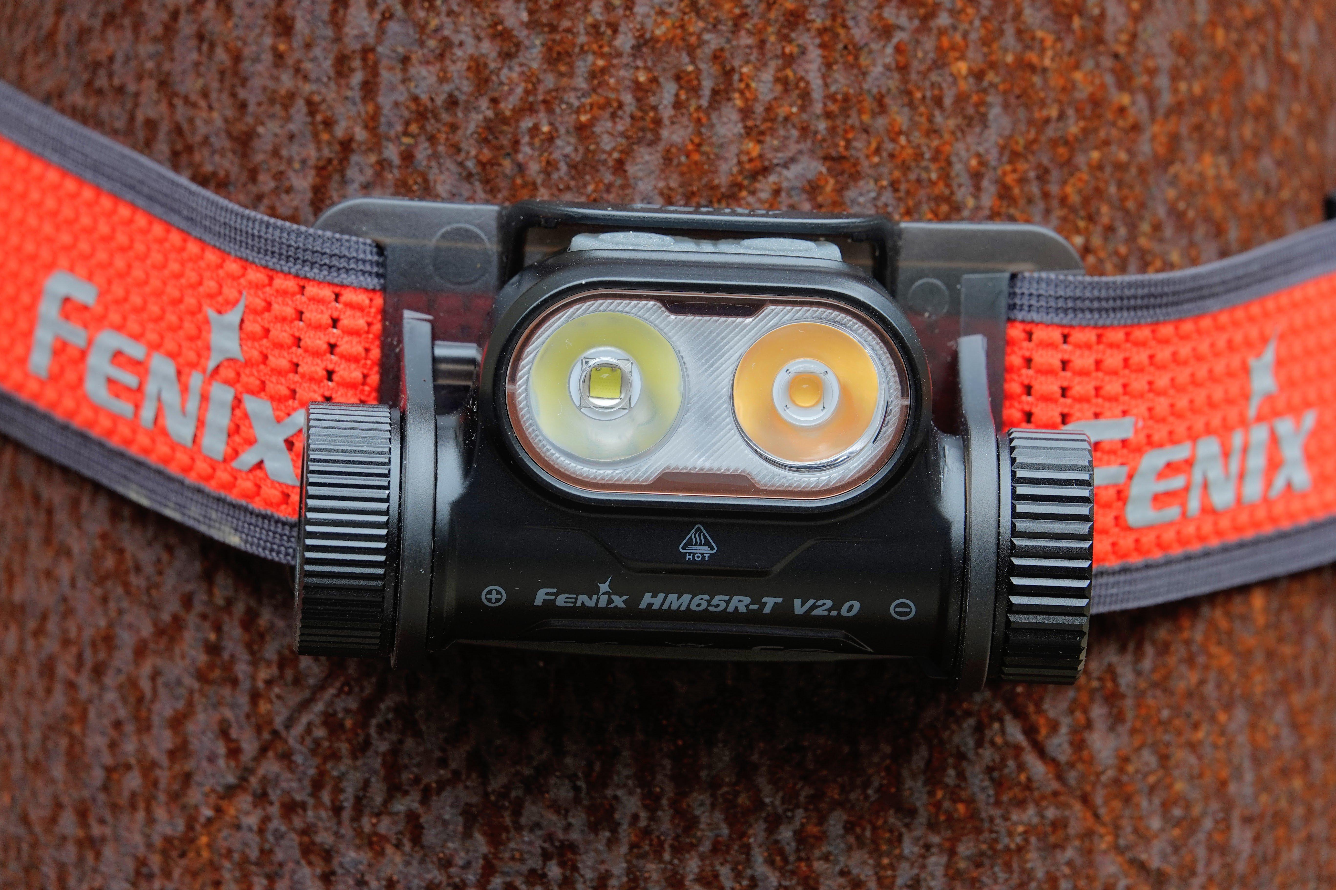 Inzoomen op de Fenix HM65R-T V2.0 zwarte hoofdlamp met rode draagriem, geplaatst op een roestig oppervlak.