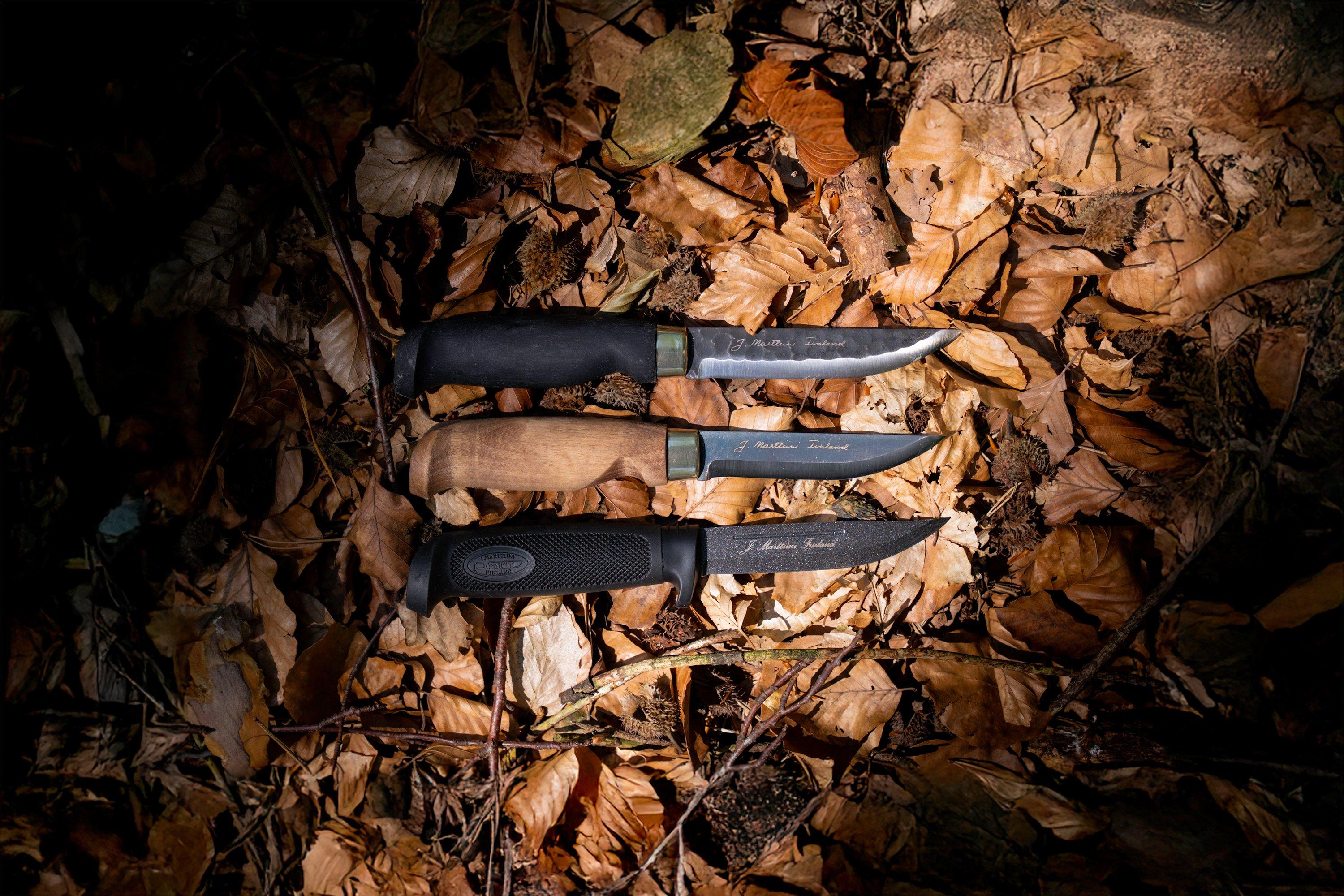 Imagen de ambiente de tres cuchillos de hoja fija Marttiini sobre un suelo cubierto de hojas en el bosque.