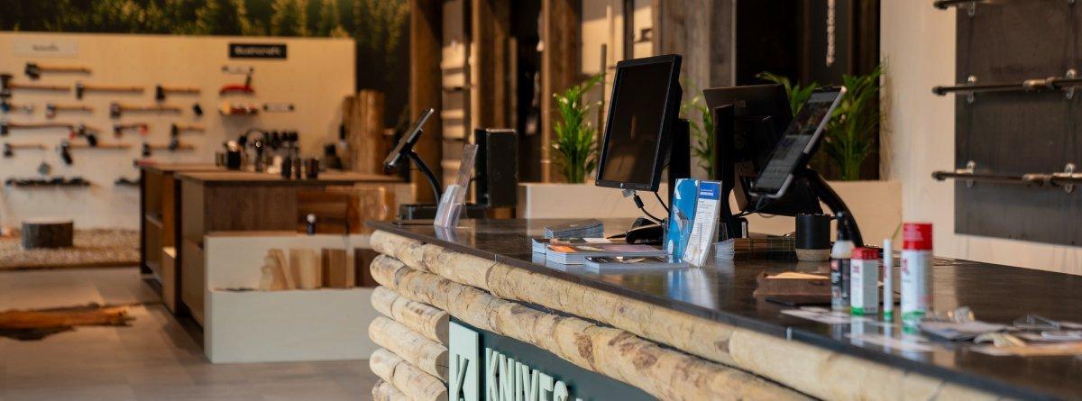 Der Kassenbereicht des Knivesandtools Experience Center. Auf der the sieht man Produkte vom Hersteller ballistol und im Hintergrund verschiedene Äxte