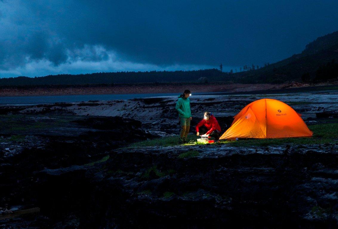 Dos personas frente a una tienda de campaña naranja utilizando linternas frontales Ledlenser