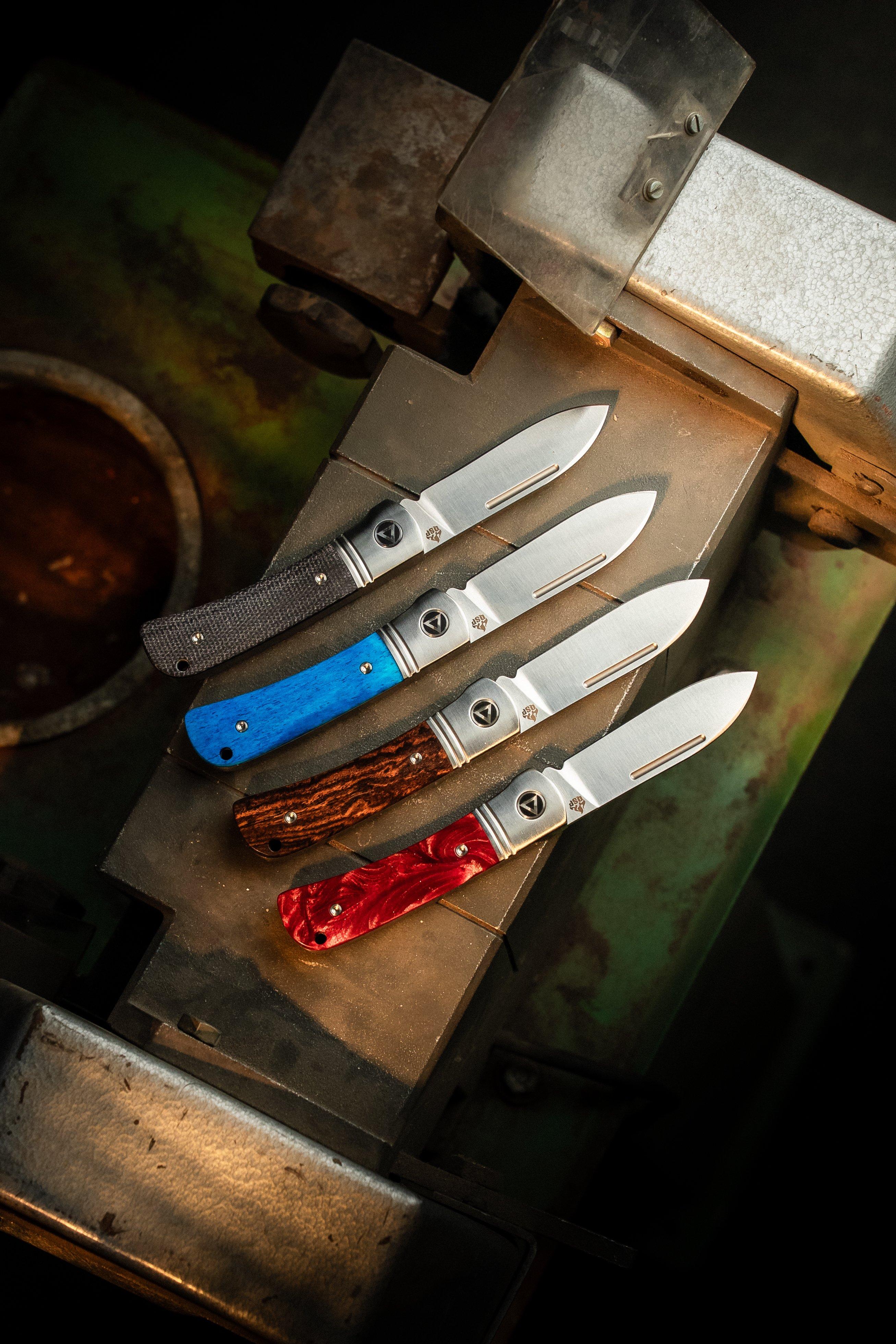 Vier QSP Hedgehog Messer mit unterschiedlichen Griffmaterialien auf einer verwitterten, farbenfrohen Oberfläche