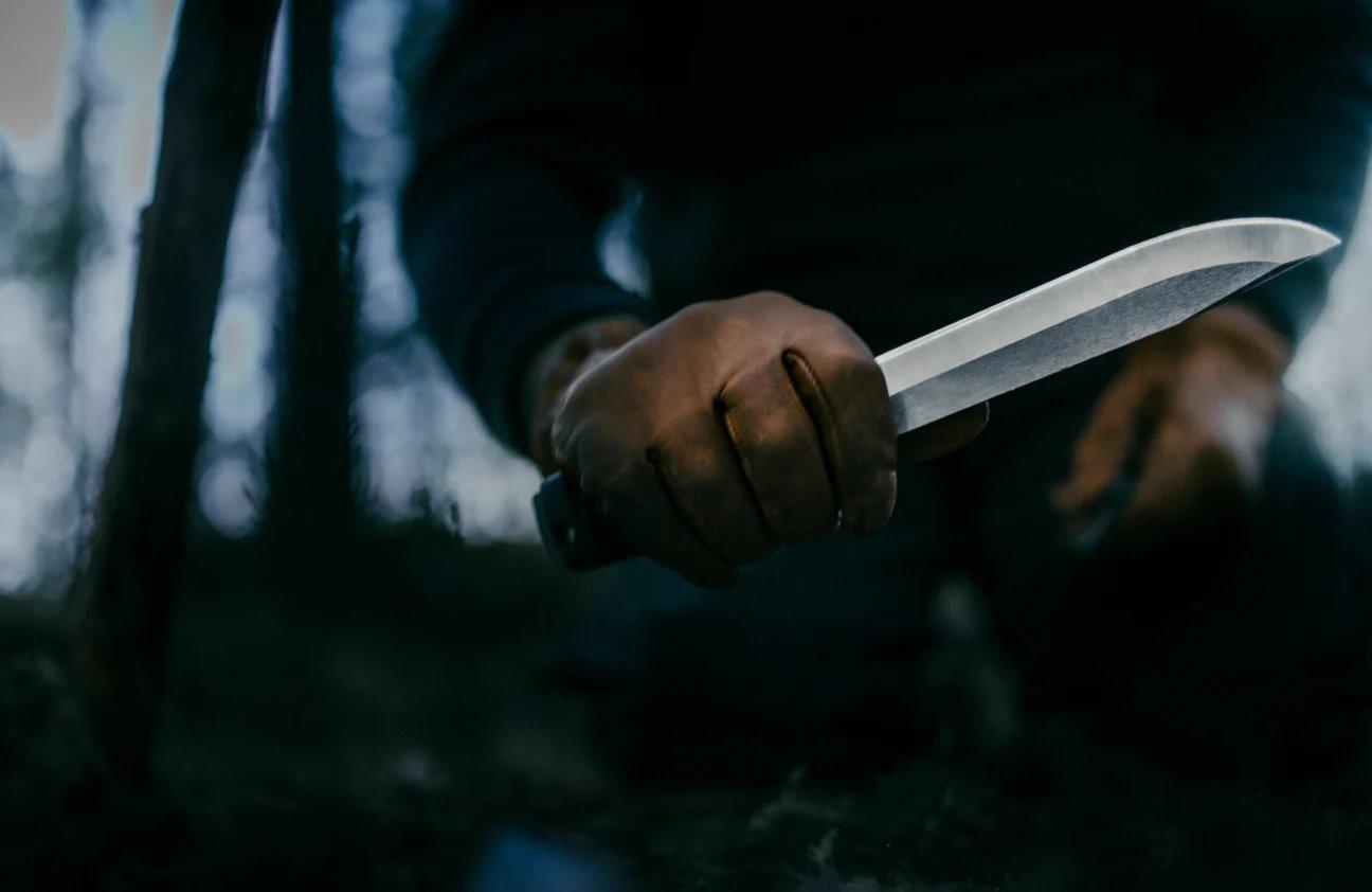 Hand met leren handschoen houdt een Morakniv Mörkret-survivalmes vast in een donker bos