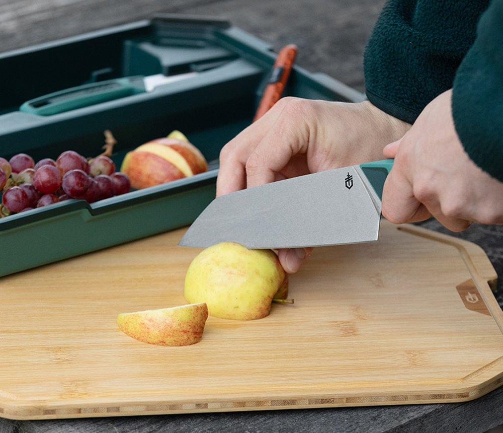 Een Gerber ComplEAT koksmes die een appel doorsnijdt op een Gerber ComplEAT snijplank.