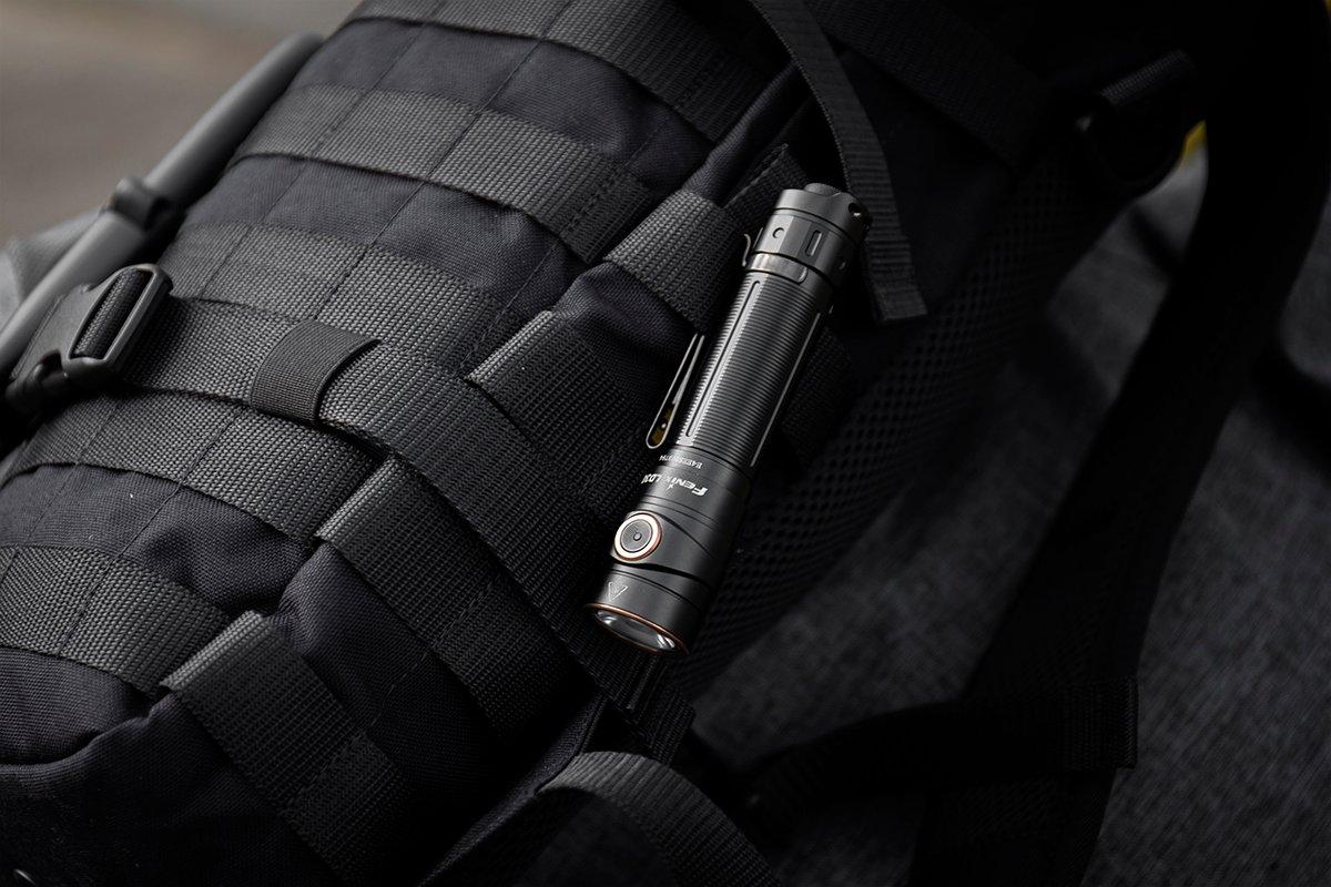 Zwarte Fenix-zaklamp met clip aan een zwarte rugzak met MOLLE-banden