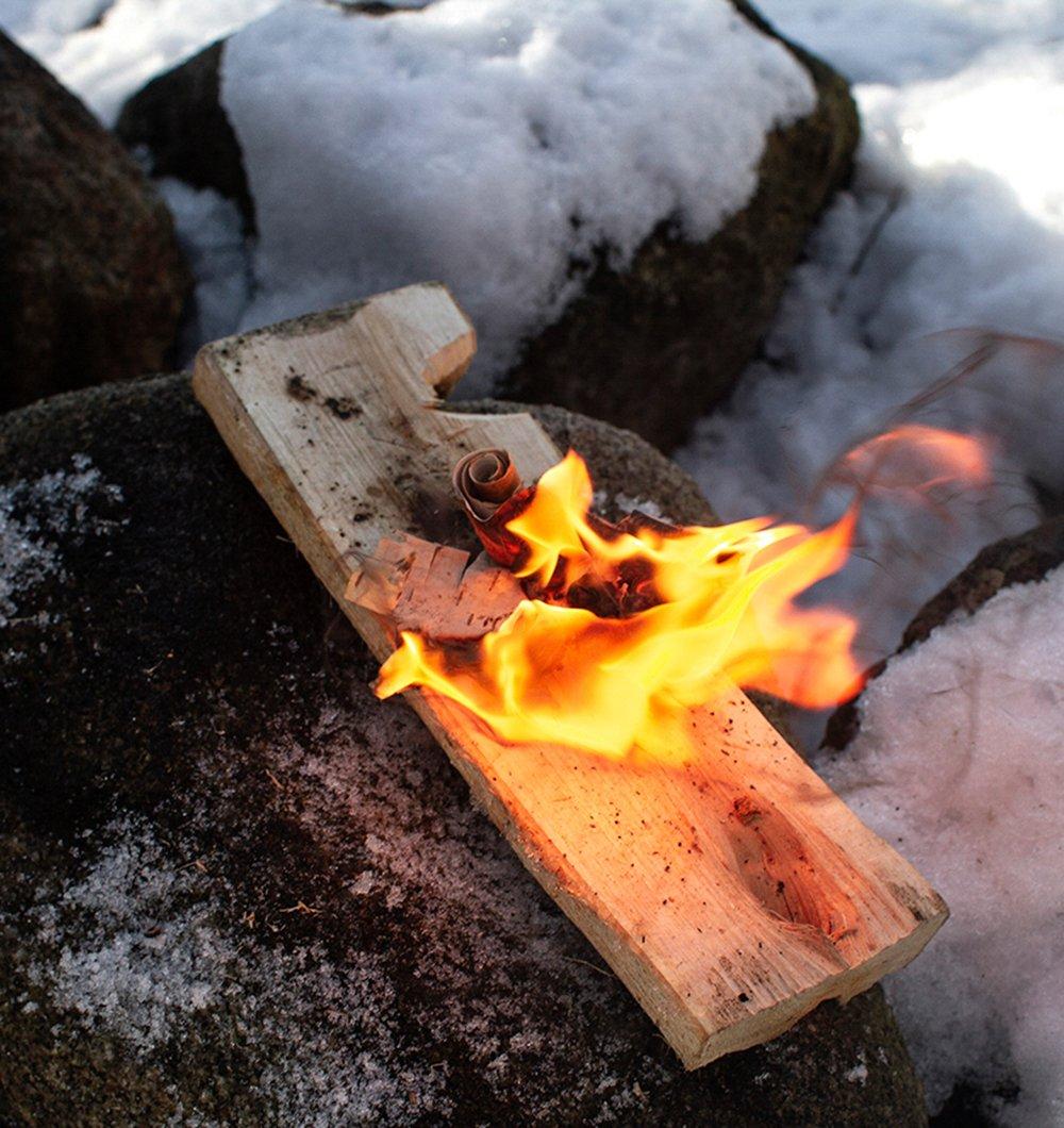 Een brandende vuurmaker met berkenbast op besneeuwde rotsen.