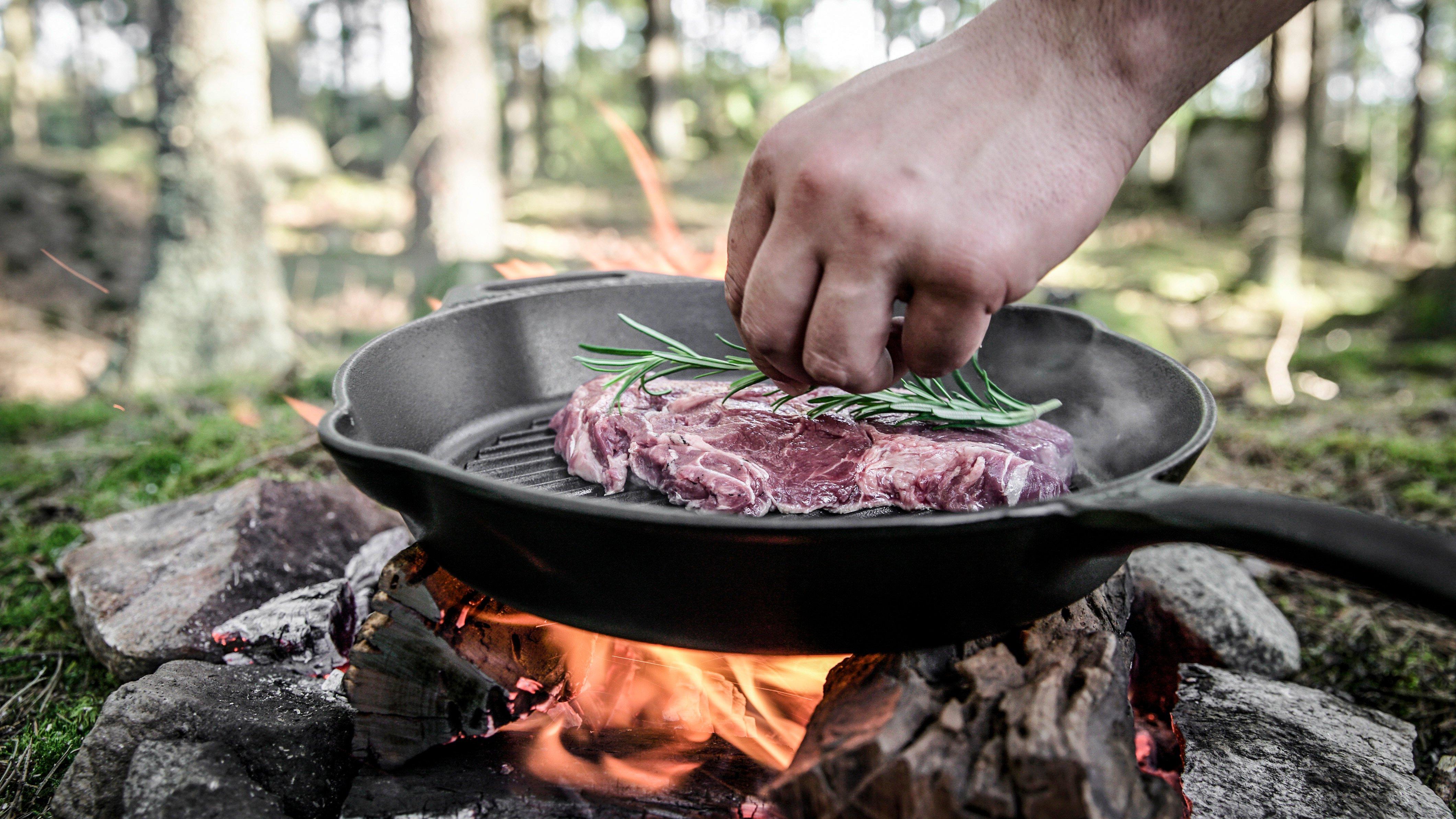 Een persoon die buiten een steak met een takje rozemarijn bakt in een gietijzeren grillpan