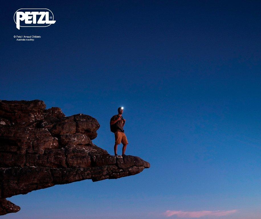 Une personne sur un rocher au tomber du jour avec une lampe frontale Petzl