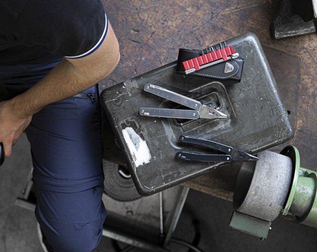 Um homem está sentado ao lado de um pedaço de metal com duas multiferramentas Victorinox e uma bolsa preta Victorinox