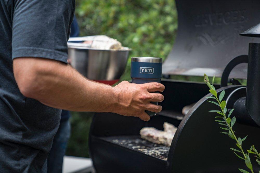 A hand holds a blue cup with the Yeti brand logo