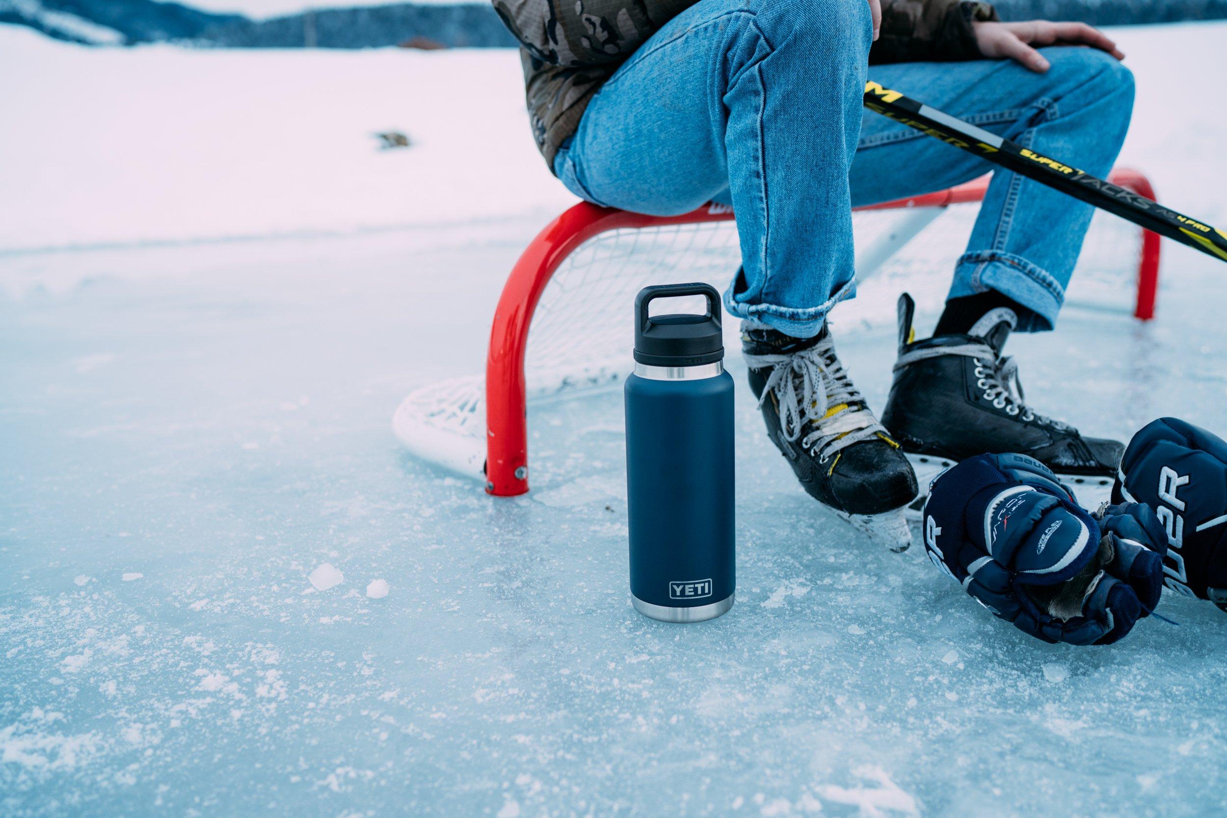 A blue Yeti Rambler bottle on an icy surface, in front of a person sitting down, wearing iceskates