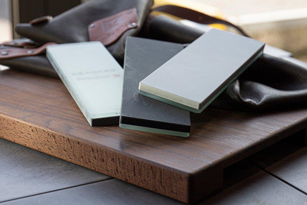 Tres piedras de afilar Zwilling de diferentes tamaños de grano en una mesa de madera