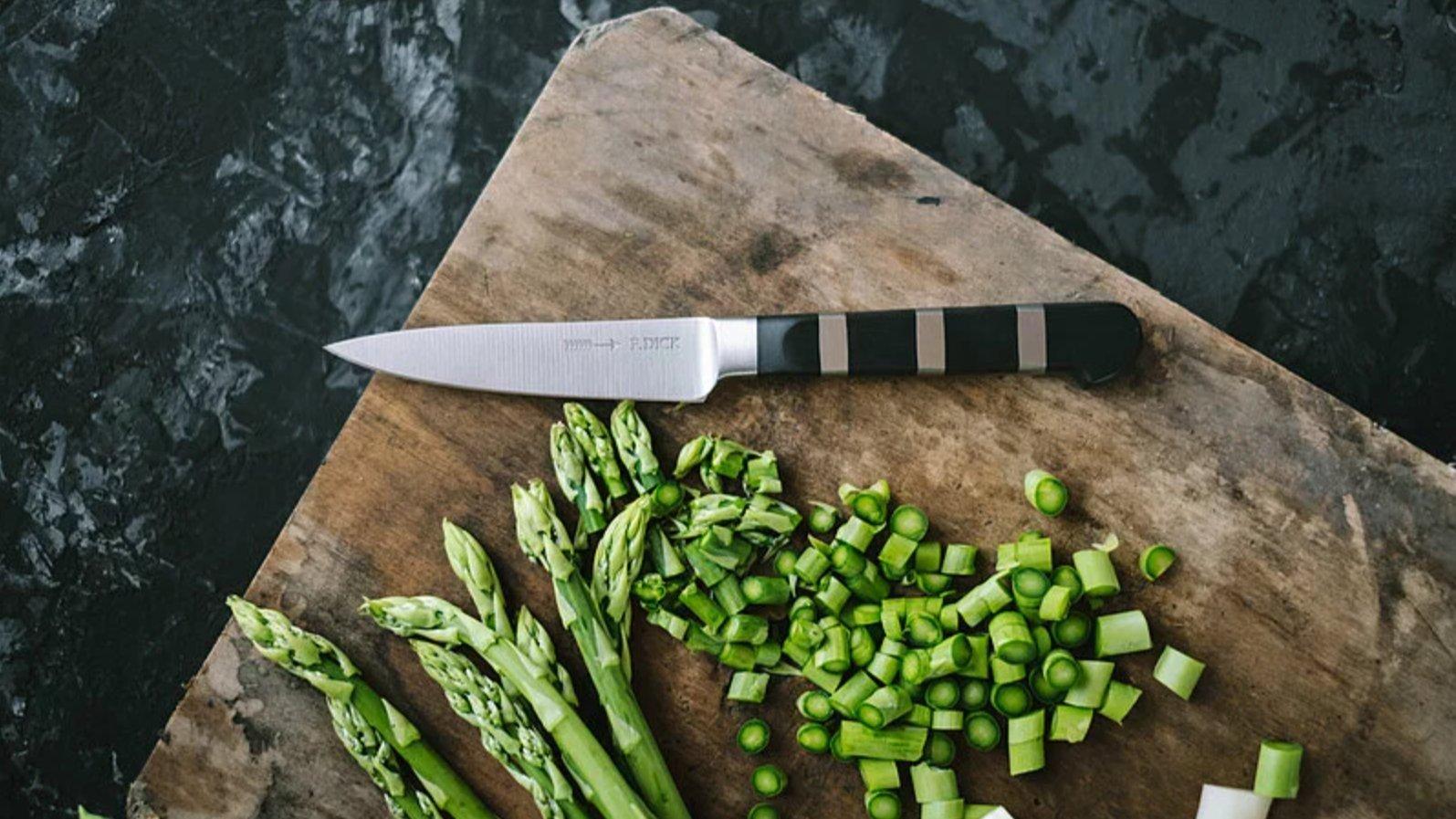 Un cuchillo puntilla F. Dick de la serie 1905 sobre una tabla de cortar de madera con espárragos verdes finamente picados
