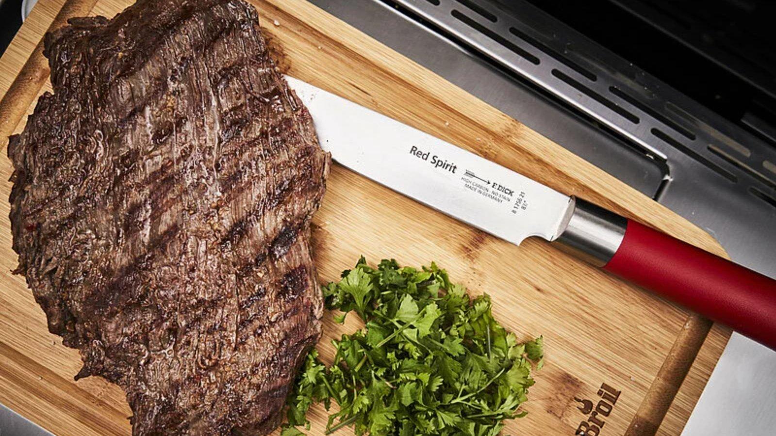 Un couteau à viande F. Dick Red Spirit sur une planche à découper en bois contre un steak cuit