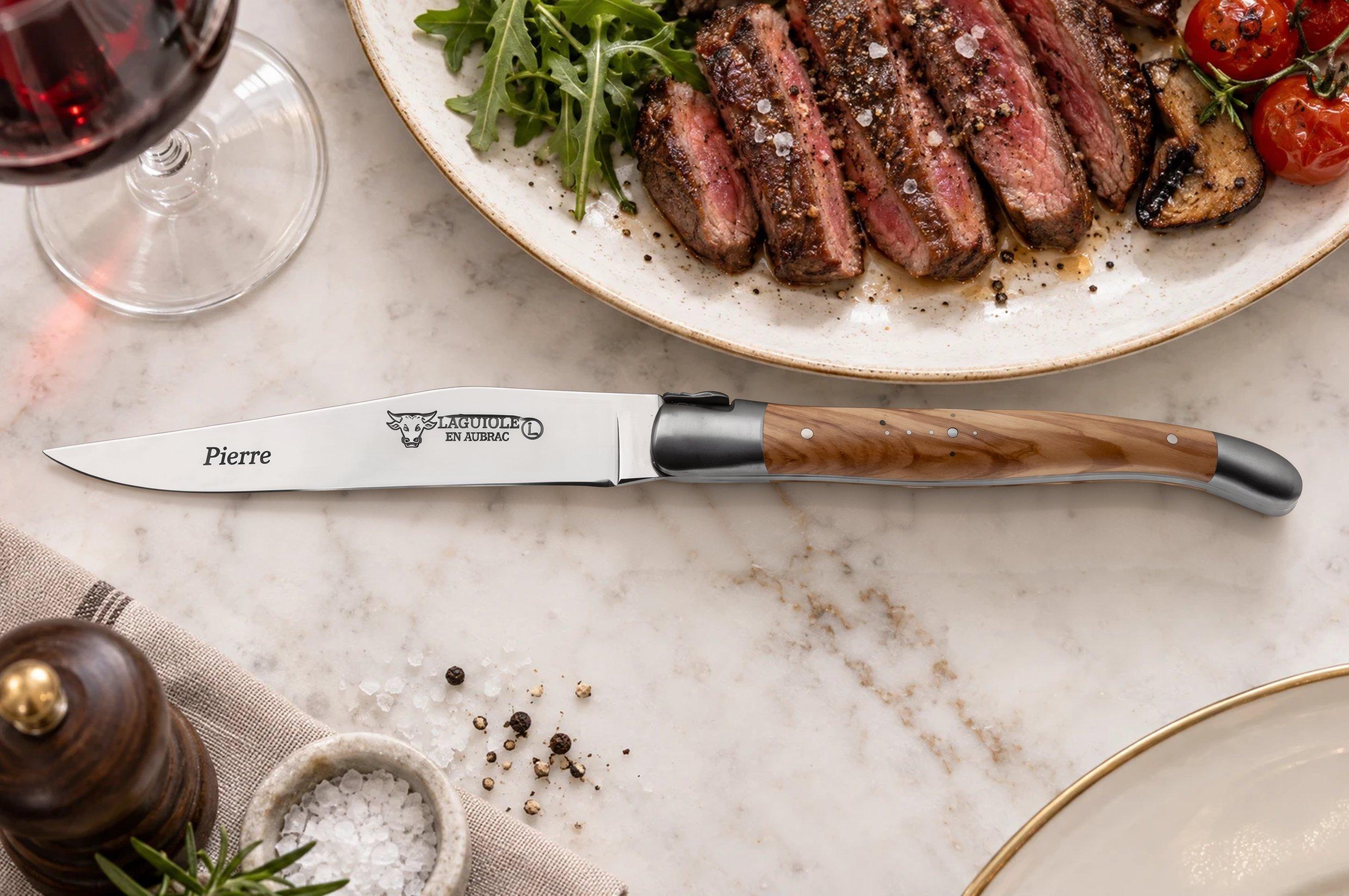 Laguiole-steakmes met olijfhouten heft en de gegraveerde naam “Pierre”, naast een bord met biefstuk