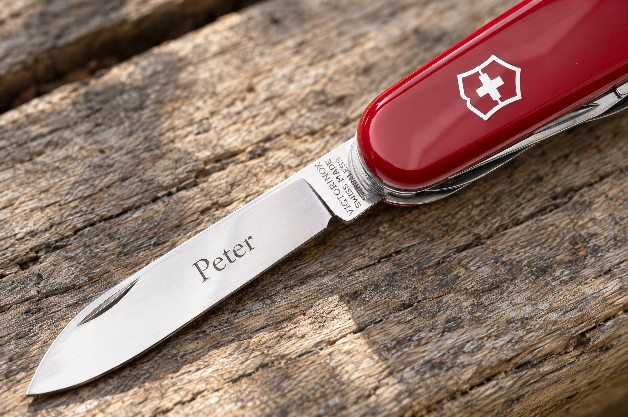 Rood Victorinox-zakmes met de naam “Peter” in het lemmet gegraveerd, op een houten balk