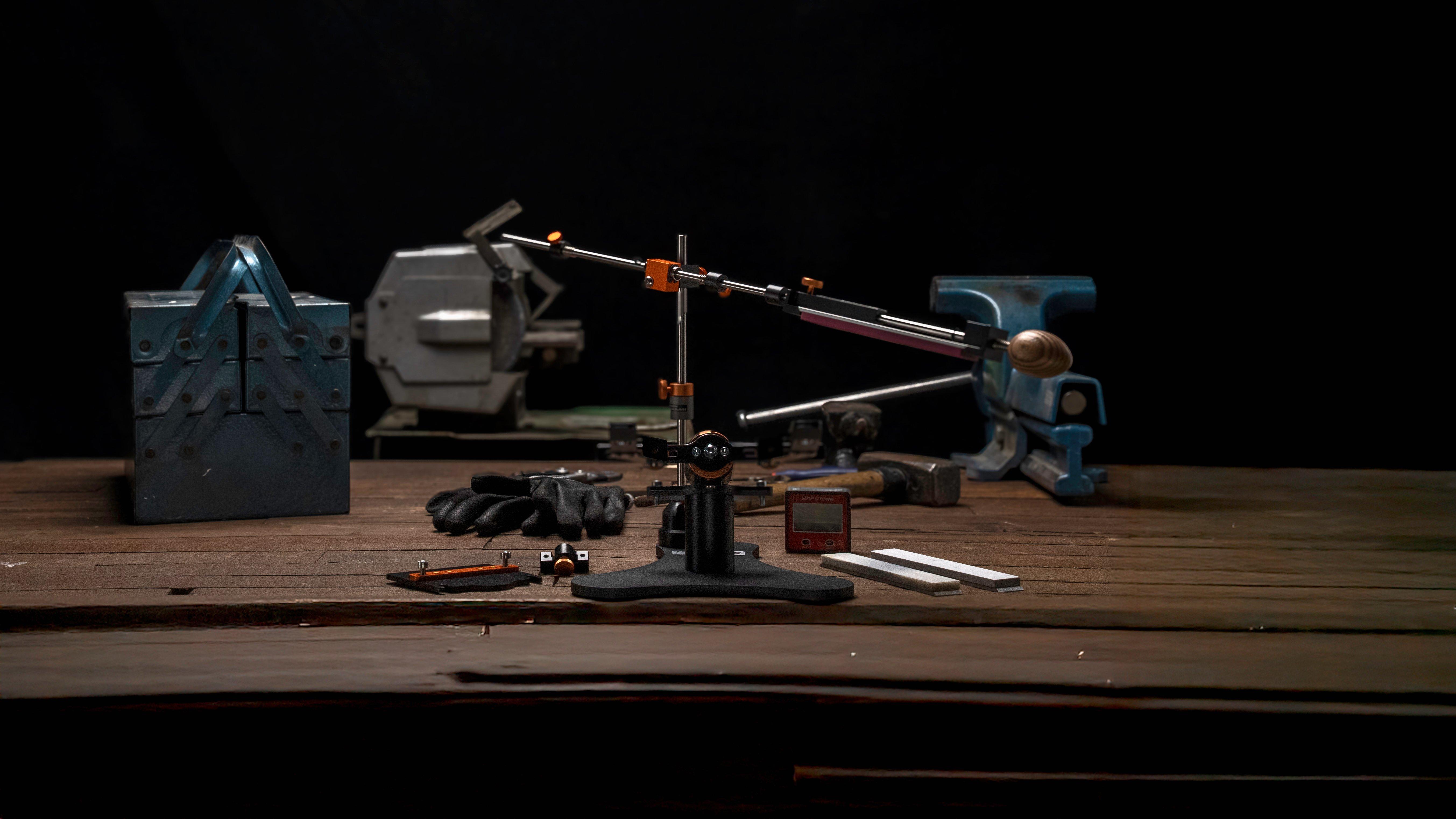 Sistema de afilado Hapstone R2 con un cuchillo de cocina en la abrazadera, fotografiado desde abajo con tablas de madera al fondo.