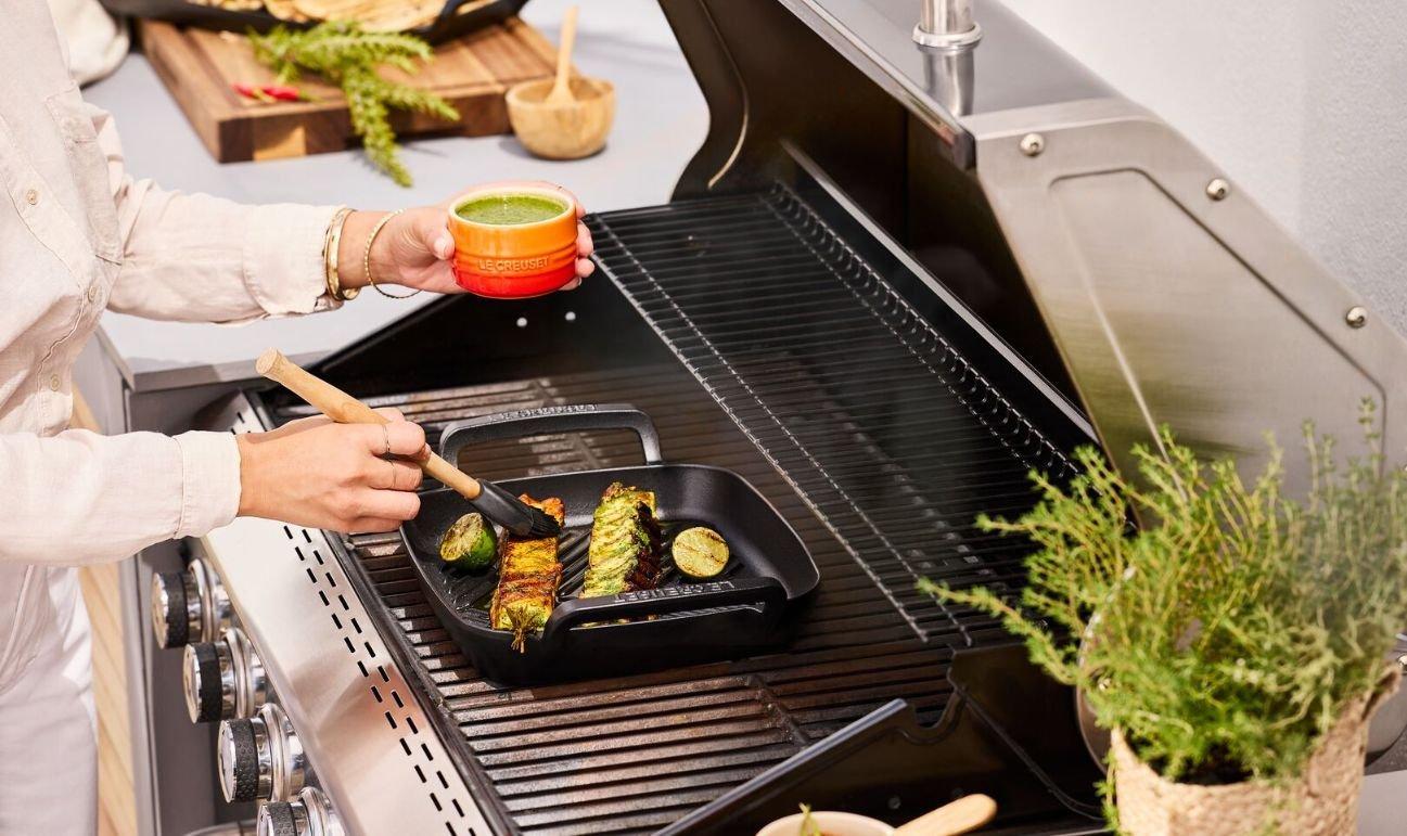 Person grillt im Freien mit einem Le Creuset BBQ Collection Bräter auf dem Grill