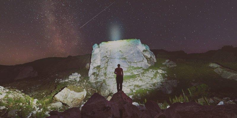 Una persona iluminando una roca con una linterna Nitecore en mitad de la noche en la montaña