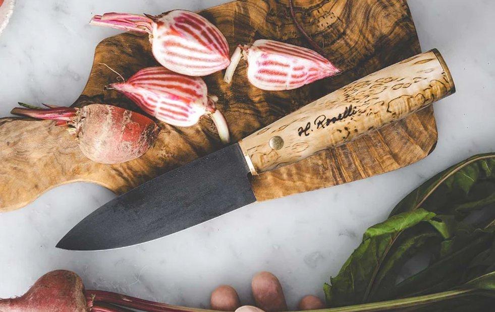 Una mesa de mármol con un cuchillo universal Roselli sobre una tabla de cortar de madera junto a remolachas Chioggia en rodajas.