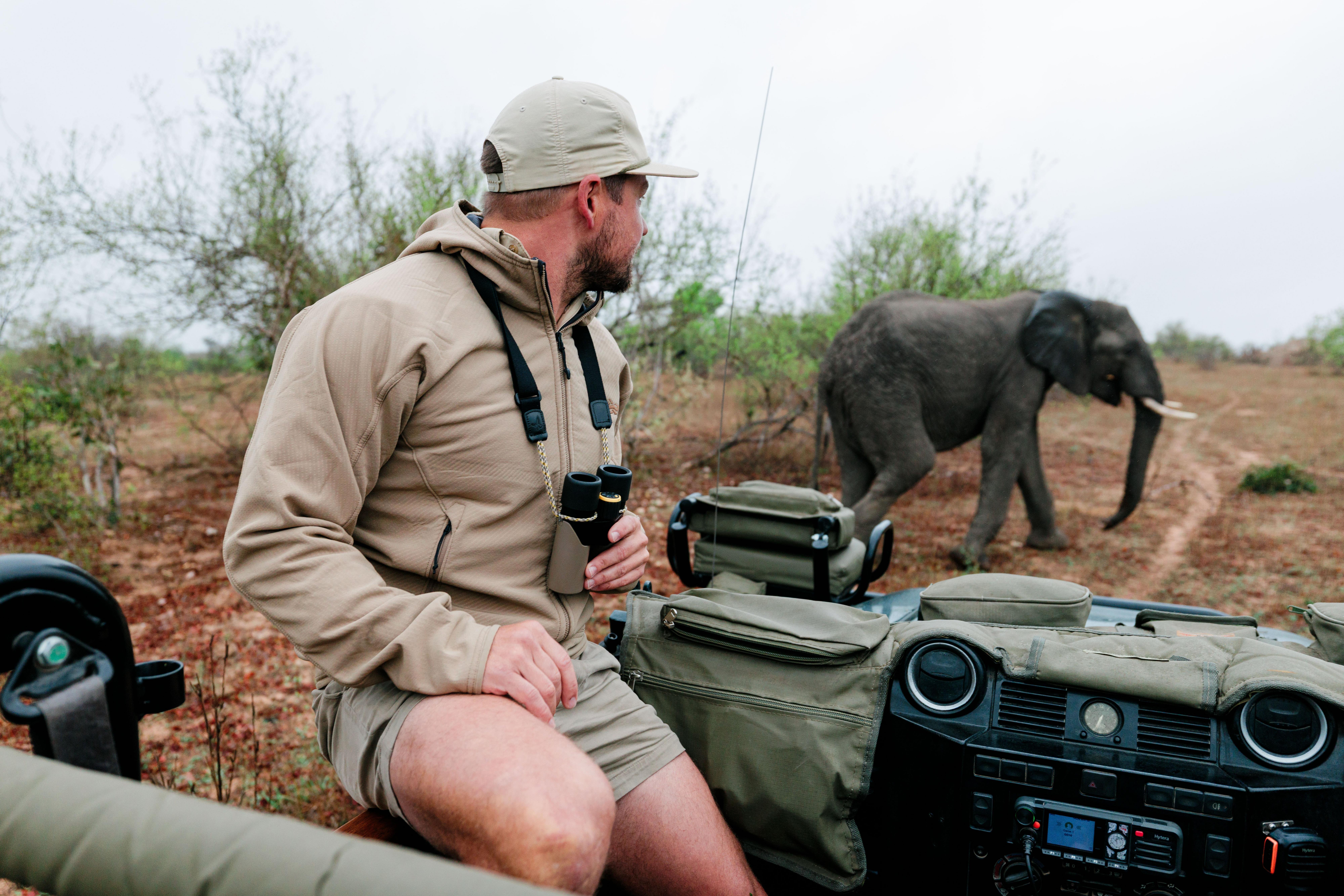 Guide on a safari vehicle with a Swarovski CL Companion around the neck, with an elephant in the background